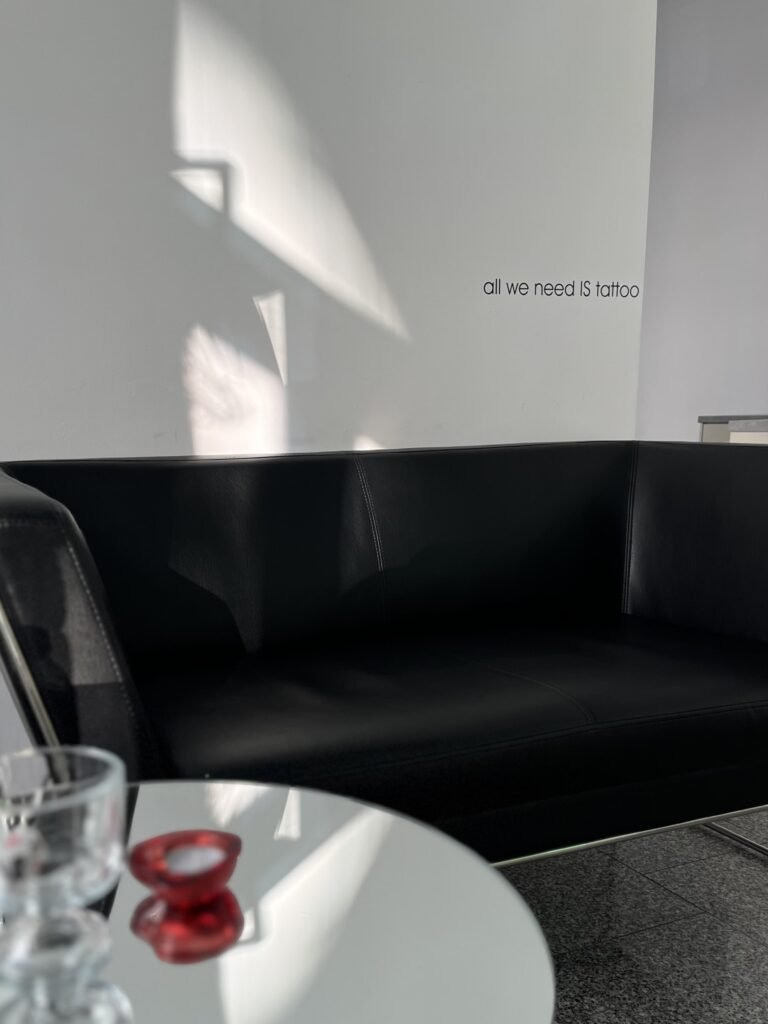 Strefa klienta w studiu Fineline Tattoo Gallery w Krakowie. Minimalistyczne wnętrze, wygodna sofa i naturalne światło tworzą spokojną, komfortową atmosferę przed i po wykonaniu tatuażu.