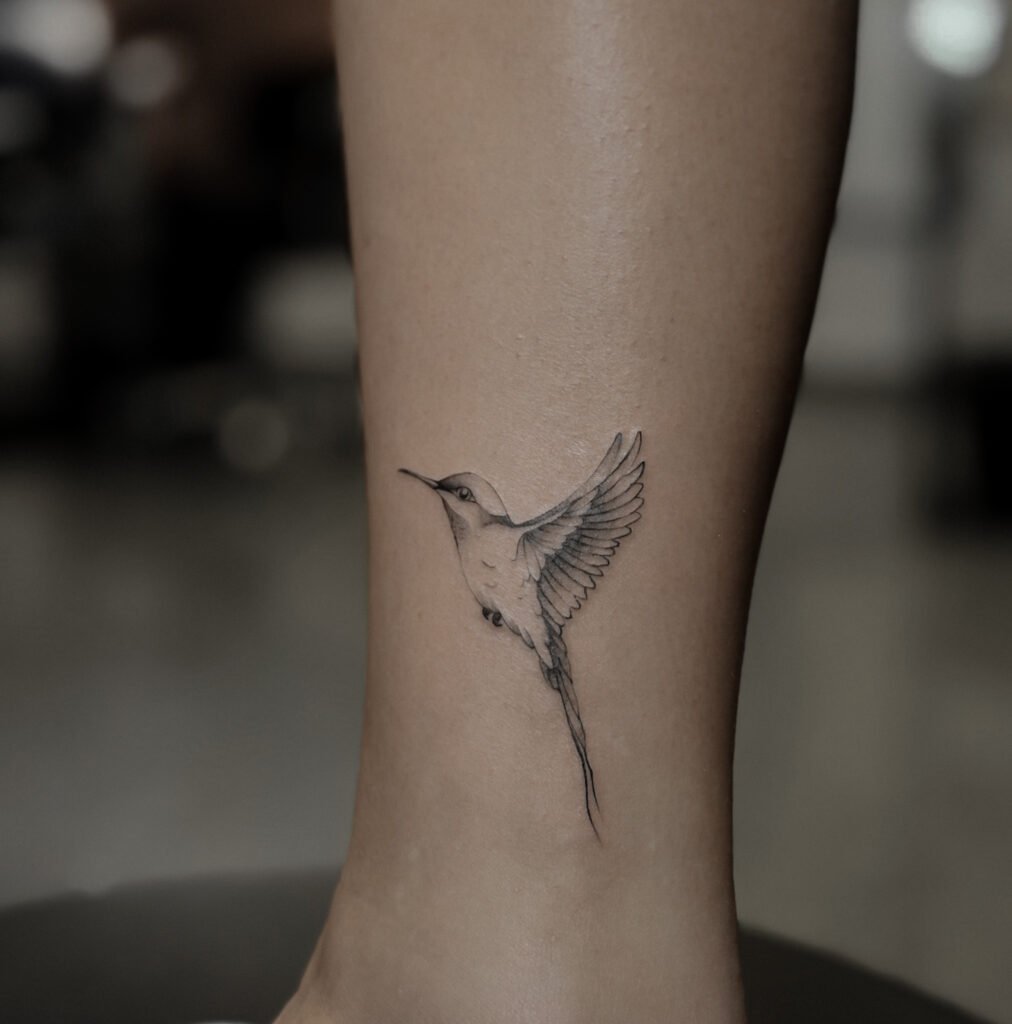 Pierwsza praca kursantki wykonana podczas szkolenia tatuażu. Delikatny tatuaż fineline przedstawiający kolibra, zrealizowany w ramach nauki technik tatuowania.